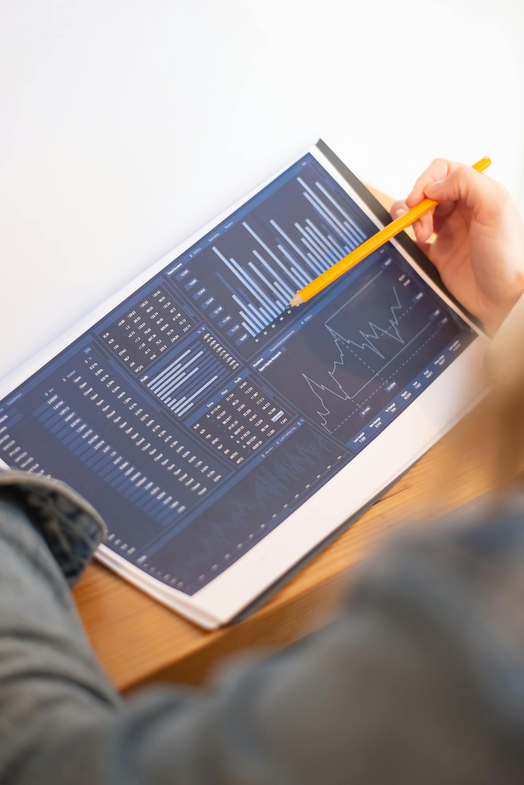 A close-up of a person analyzing blue graph data with a yellow pencil.